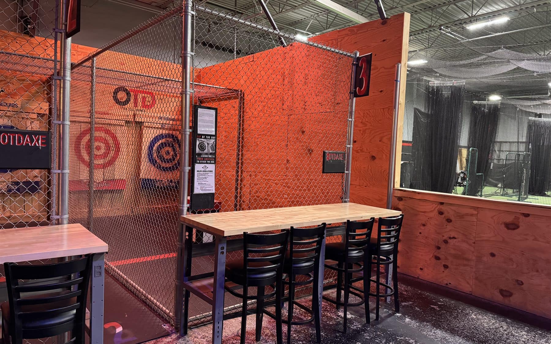 Axe throwing lane seating beside fenced throwing stalls at On The Dunes Sports in Commerce Township
