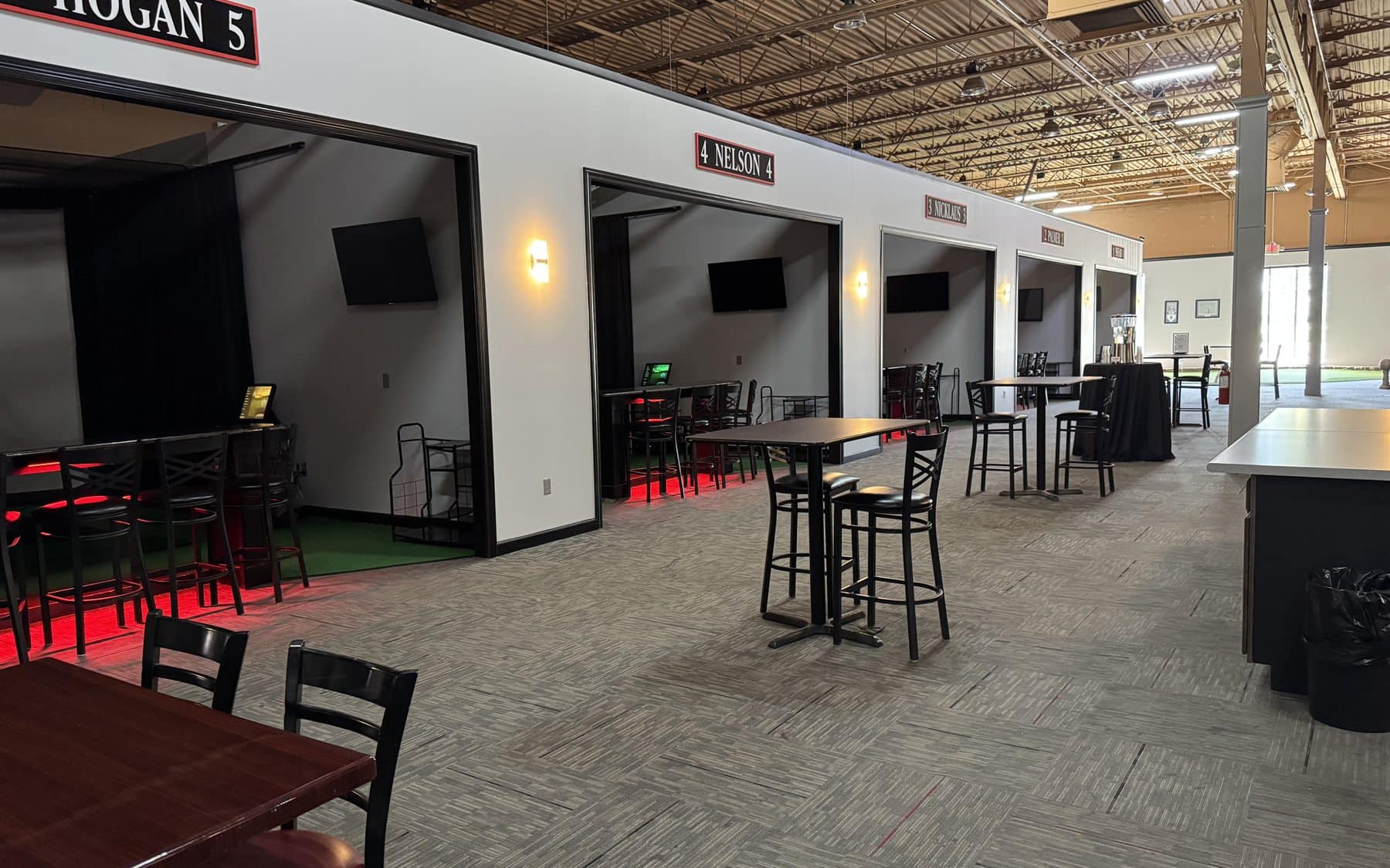 Row of HD Golf simulator bays with tables and seating at On The Dunes Sports
